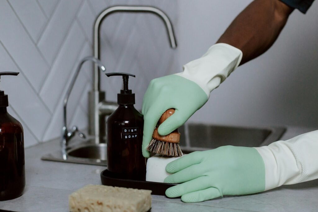 Hands in latex gloves washing dishes with soap at a kitchen sink.